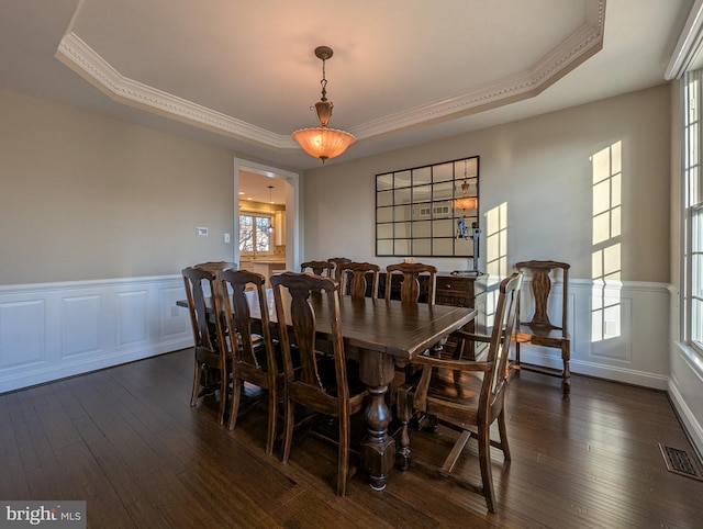 dining space featuring a raised ceiling, ornamental molding, and dark wood-type flooring