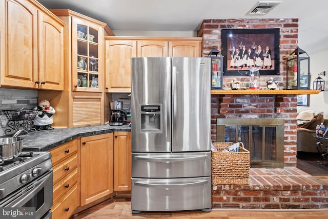 kitchen featuring a brick fireplace, light wood-type flooring, stainless steel appliances, and tasteful backsplash