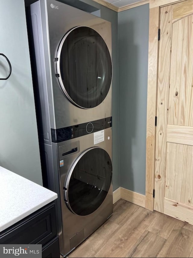 washroom featuring cabinets, light hardwood / wood-style flooring, stacked washer and clothes dryer, and crown molding