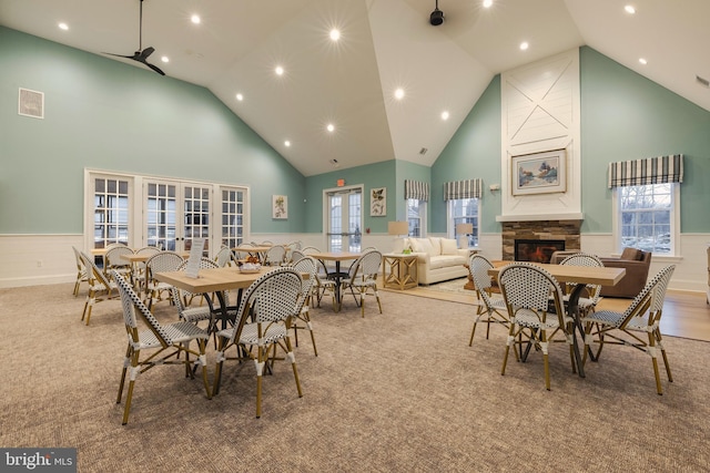 dining room featuring high vaulted ceiling, light colored carpet, and a stone fireplace