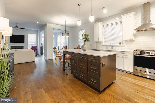 kitchen with hanging light fixtures, gas stove, a kitchen island, white cabinets, and wall chimney range hood