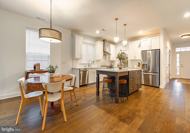 kitchen with white cabinets, appliances with stainless steel finishes, wall chimney exhaust hood, and hanging light fixtures