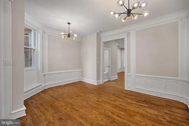 unfurnished dining area featuring wood-type flooring, an inviting chandelier, and ornamental molding