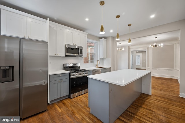 kitchen with sink, dark wood-type flooring, stainless steel appliances, decorative light fixtures, and white cabinets