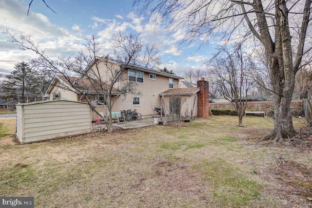 rear view of house featuring a chimney, a storage unit, a lawn, fence, and an outdoor structure