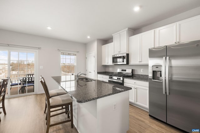 kitchen featuring light hardwood / wood-style flooring, an island with sink, white cabinetry, dark stone counters, and appliances with stainless steel finishes