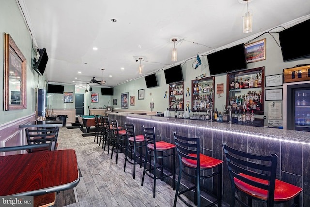 bar featuring ceiling fan, wood-type flooring, crown molding, and beverage cooler