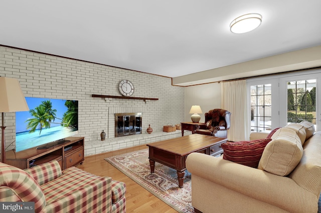 living room featuring french doors, a brick fireplace, brick wall, and light hardwood / wood-style flooring