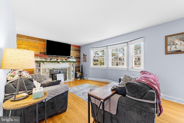 living area featuring an accent wall, wood walls, wood finished floors, visible vents, and baseboards