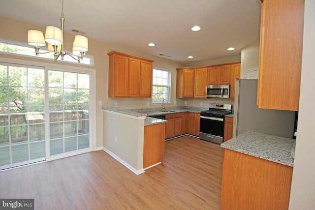 kitchen featuring sink, stainless steel appliances, an inviting chandelier, light stone counters, and decorative light fixtures