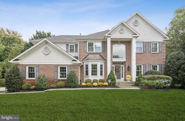 neoclassical / greek revival house featuring a front lawn, brick siding, and stucco siding