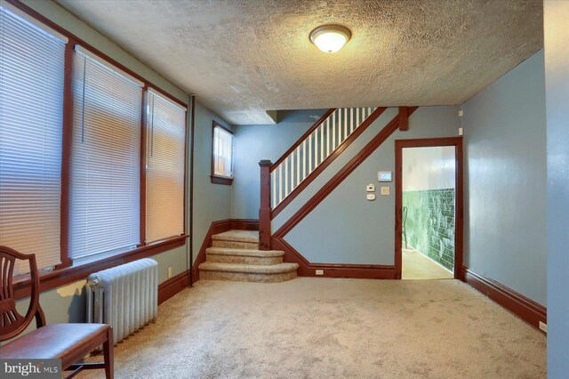 stairs featuring carpet flooring, radiator heating unit, and a textured ceiling