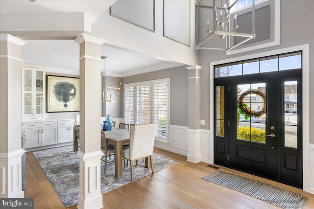 foyer entrance with ornate columns, an inviting chandelier, light wood-type flooring, and crown molding