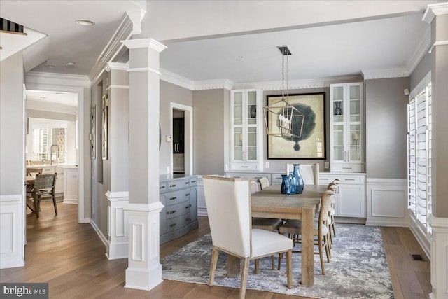 dining space featuring hardwood / wood-style floors, crown molding, and decorative columns