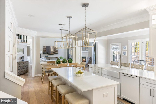 kitchen with dishwasher, hanging light fixtures, a center island with sink, white cabinets, and a kitchen breakfast bar