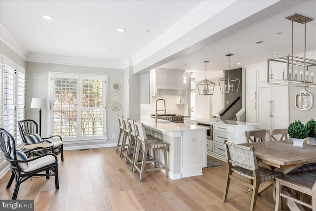 dining room featuring sink, ornamental molding, and light hardwood / wood-style flooring