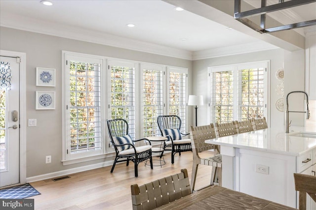 living area with ornamental molding, light hardwood / wood-style floors, a wealth of natural light, and sink