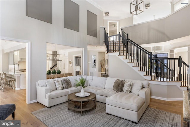 living room with a chandelier, ornamental molding, a high ceiling, light hardwood / wood-style flooring, and sink