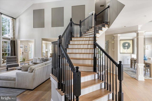 staircase featuring a high ceiling, ornamental molding, hardwood / wood-style flooring, and a notable chandelier