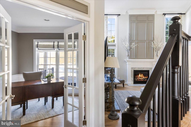 interior space with light hardwood / wood-style floors, french doors, crown molding, and a high end fireplace