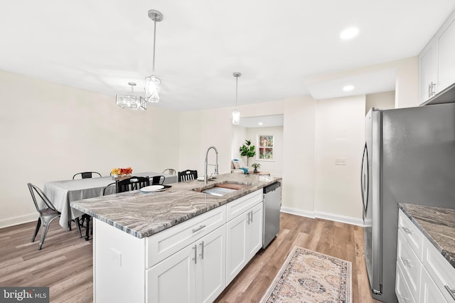 kitchen with light stone counters, light wood finished floors, appliances with stainless steel finishes, white cabinetry, and a sink