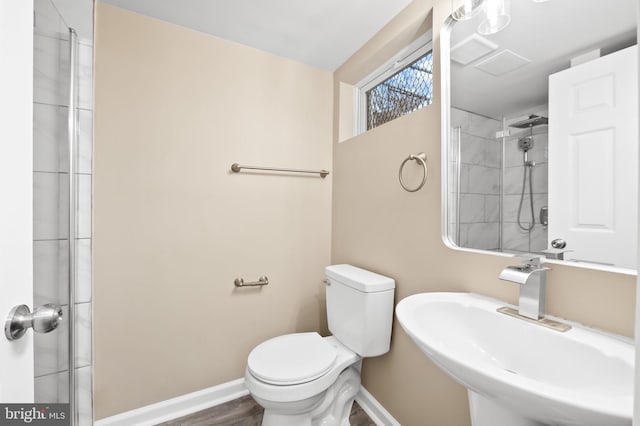 full bathroom featuring toilet, wood finished floors, a sink, baseboards, and a tile shower