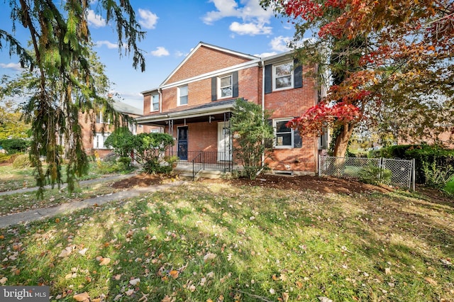 traditional home with covered porch, fence, a front lawn, and brick siding