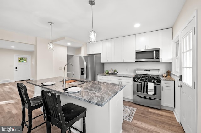 kitchen featuring light stone counters, stainless steel appliances, visible vents, white cabinets, and light wood-style floors