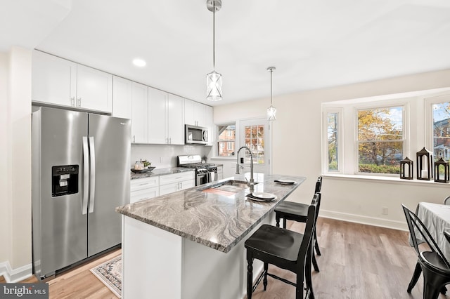 kitchen featuring a sink, light wood-style floors, white cabinets, appliances with stainless steel finishes, and light stone countertops