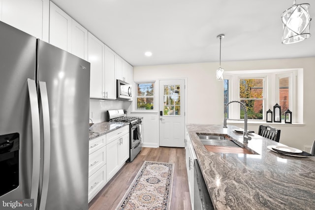 kitchen with stone counters, a sink, white cabinets, appliances with stainless steel finishes, and light wood finished floors