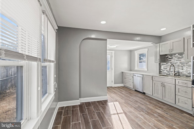 kitchen featuring gray cabinets, decorative backsplash, dishwasher, light stone counters, and sink