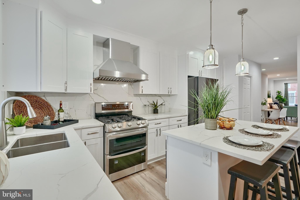 kitchen featuring white cabinets, stainless steel appliances, wall chimney range hood, and sink