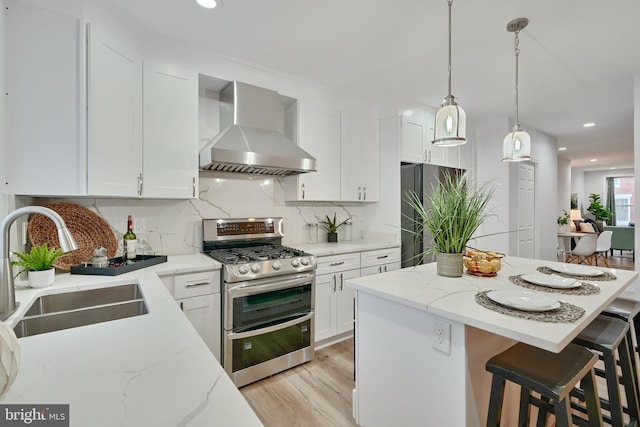 kitchen featuring white cabinets, stainless steel appliances, wall chimney range hood, and sink