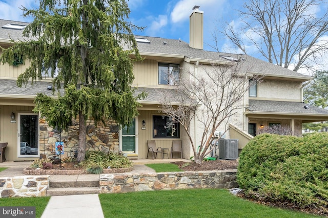 back of property with stone siding, central AC, a chimney, and a shingled roof