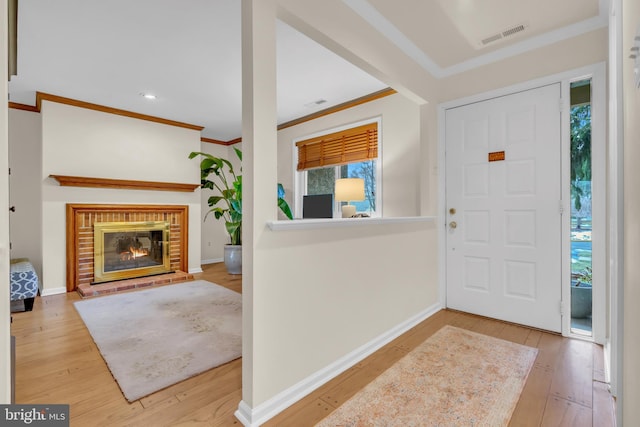 foyer entrance with a fireplace, ornamental molding, and light hardwood / wood-style floors