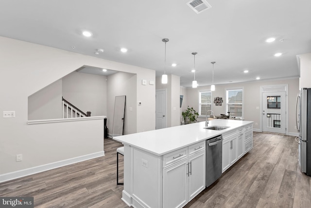 kitchen with decorative light fixtures, stainless steel appliances, a kitchen island with sink, white cabinetry, and sink