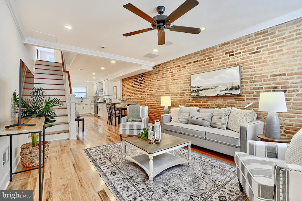 living room with light wood-type flooring, ceiling fan, crown molding, and brick wall