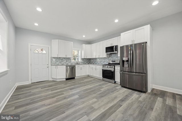 kitchen with sink, white cabinetry, light hardwood / wood-style flooring, stainless steel appliances, and decorative backsplash