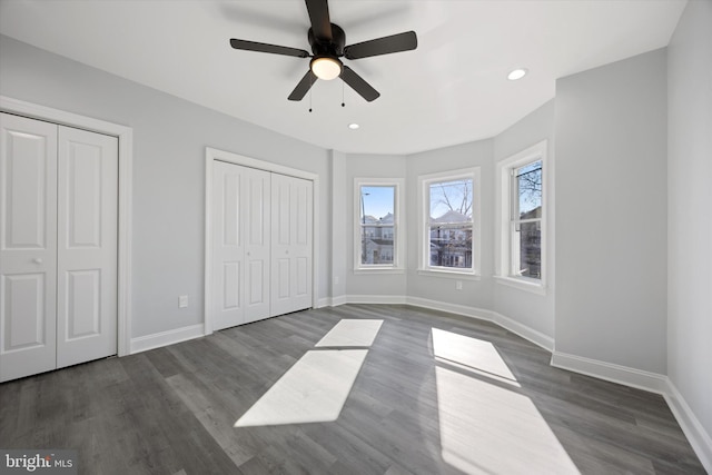 unfurnished bedroom featuring dark wood-type flooring, two closets, and ceiling fan