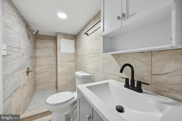 bathroom with tile walls, vanity, toilet, and tiled shower