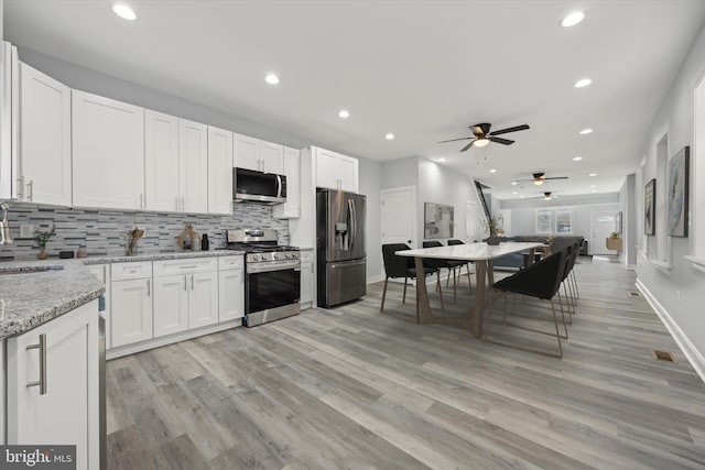 kitchen with light stone counters, appliances with stainless steel finishes, backsplash, and white cabinets