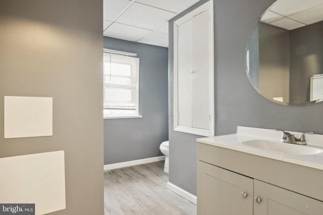 bathroom featuring toilet, hardwood / wood-style floors, a drop ceiling, and vanity