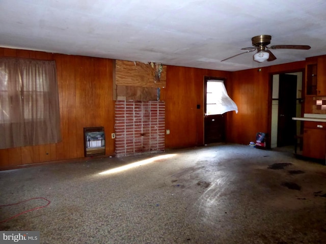 unfurnished living room featuring ceiling fan, heating unit, and wooden walls