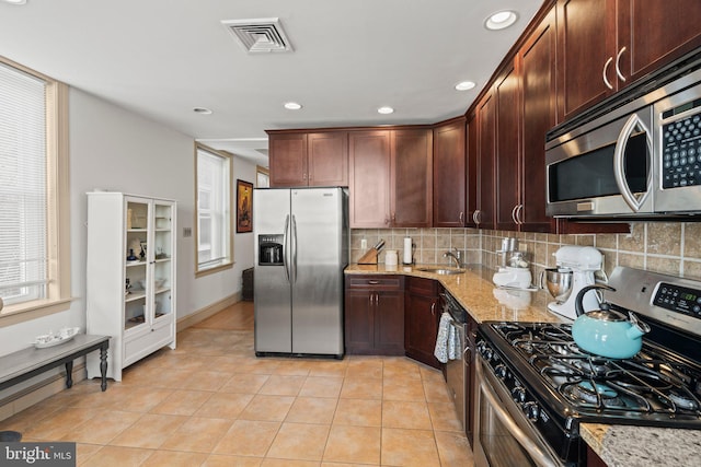 kitchen featuring light stone countertops, sink, stainless steel appliances, decorative backsplash, and light tile patterned floors