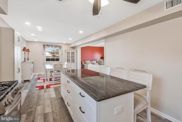 kitchen featuring a kitchen island, white cabinets, stainless steel gas stove, and a kitchen breakfast bar