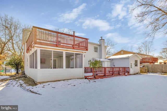 snow covered property with a deck, a sunroom, and a shed