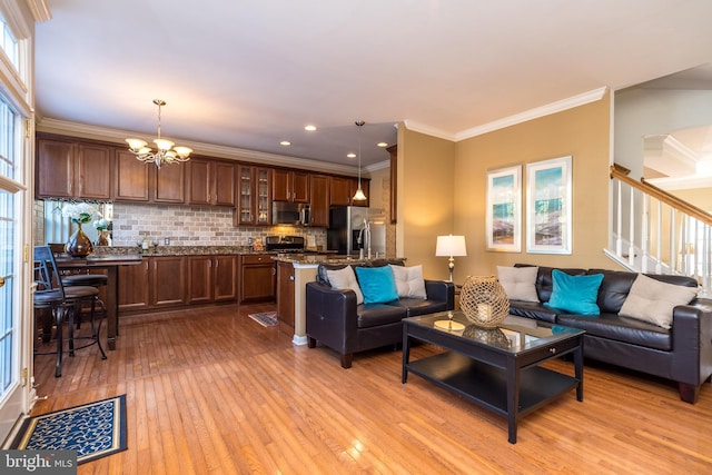 living room featuring an inviting chandelier, crown molding, and light wood-type flooring