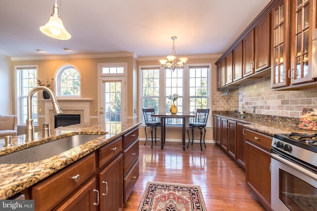 kitchen featuring a wealth of natural light, decorative light fixtures, sink, light stone counters, and gas range