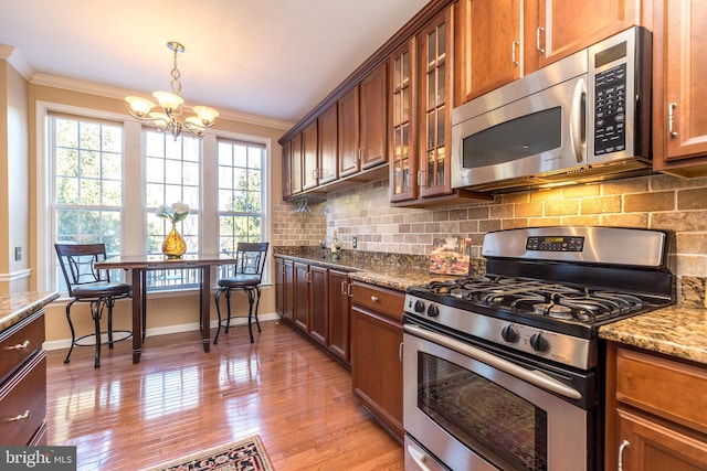 kitchen with tasteful backsplash, hanging light fixtures, ornamental molding, light stone counters, and stainless steel appliances