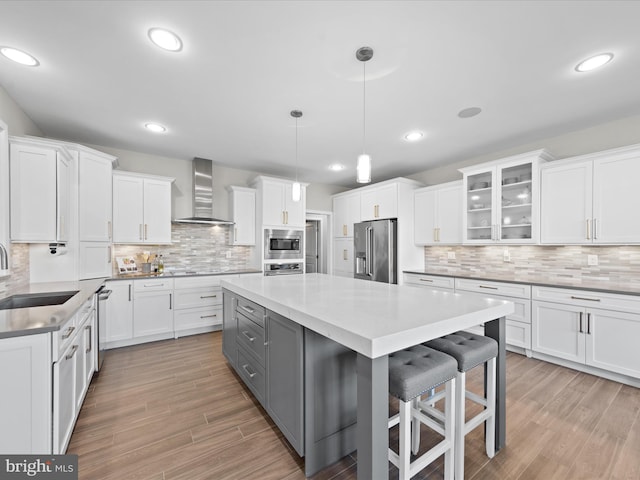 kitchen featuring white cabinets, wall chimney exhaust hood, a breakfast bar, stainless steel appliances, and light countertops